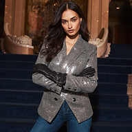A person wears a silver Kyomi Sequined Blazer and black leather gloves while standing with arms crossed in front of a blue carpeted staircase.