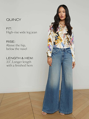 A woman indoors wears the Quincy Wide-Leg Jean—crafted from 100% cotton denim with a high rise that sits above the hip and below the navel, plus a wide leg and a 33-inch hem—paired with a vibrant patterned blouse.