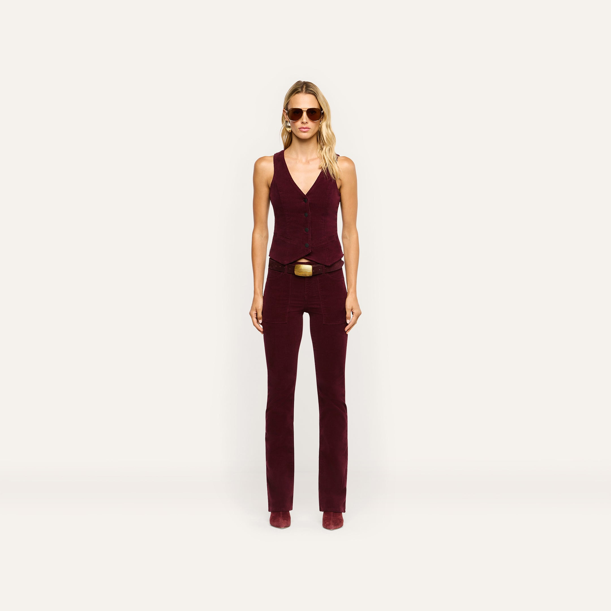 A person wearing a tailored burgundy Yelena Corduroy Vest and matching stretch corduroy pants with a belt.