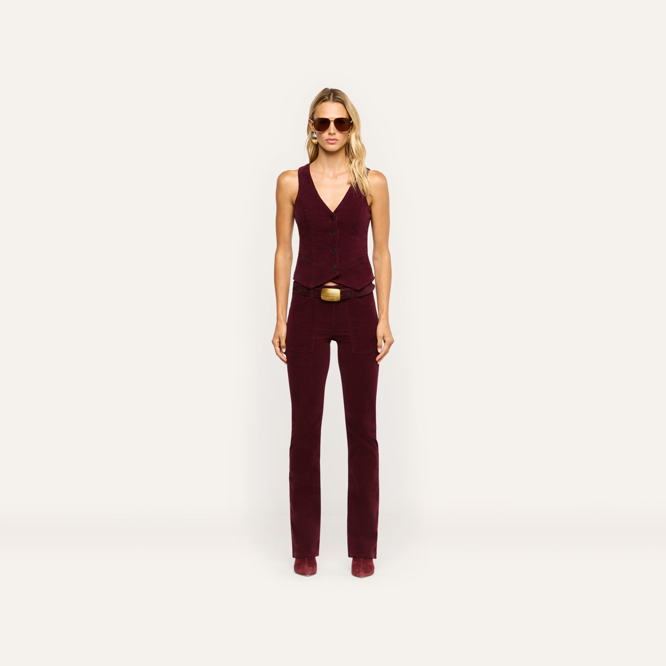 A person wearing a tailored burgundy Yelena Corduroy Vest and matching stretch corduroy pants with a belt.