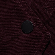 Close-up of the Yelena Corduroy Vest in dark burgundy stretch corduroy, featuring a single circular black button embossed with text.