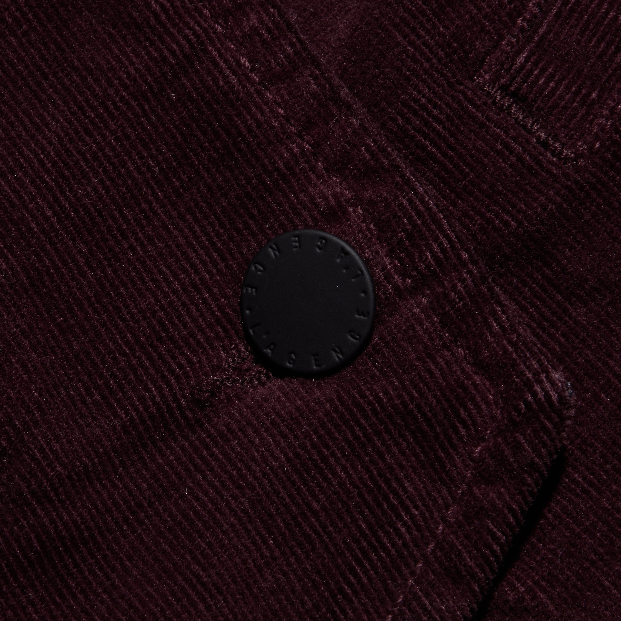Close-up of the Yelena Corduroy Vest in dark burgundy stretch corduroy, featuring a single circular black button embossed with text.
