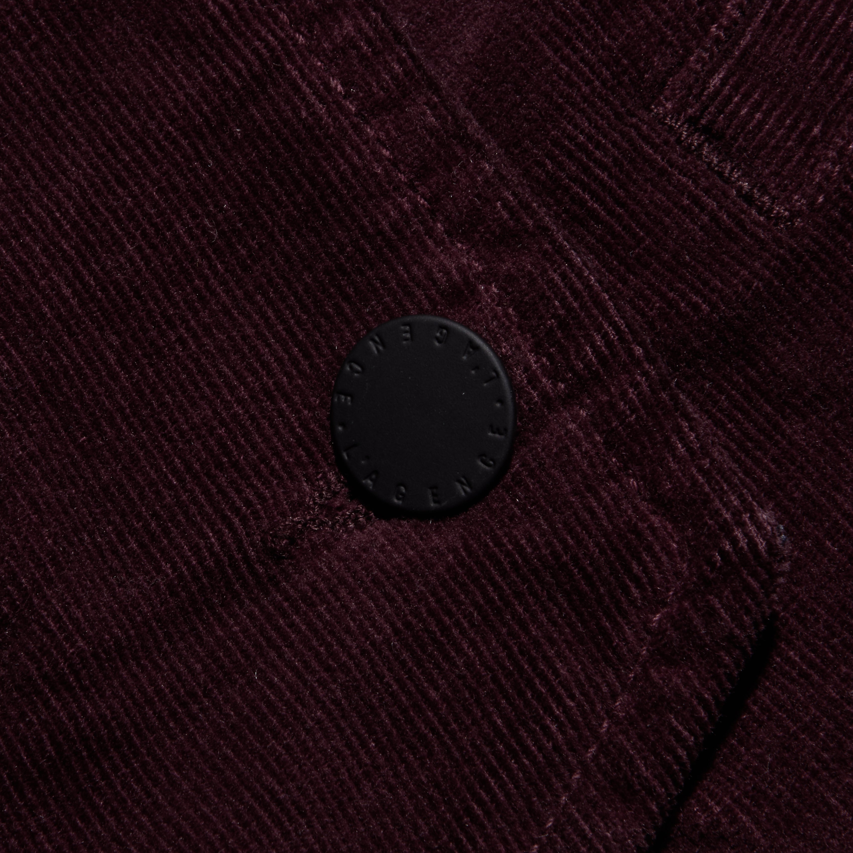 Close-up of the Yelena Corduroy Vest in dark burgundy stretch corduroy, featuring a single circular black button embossed with text.