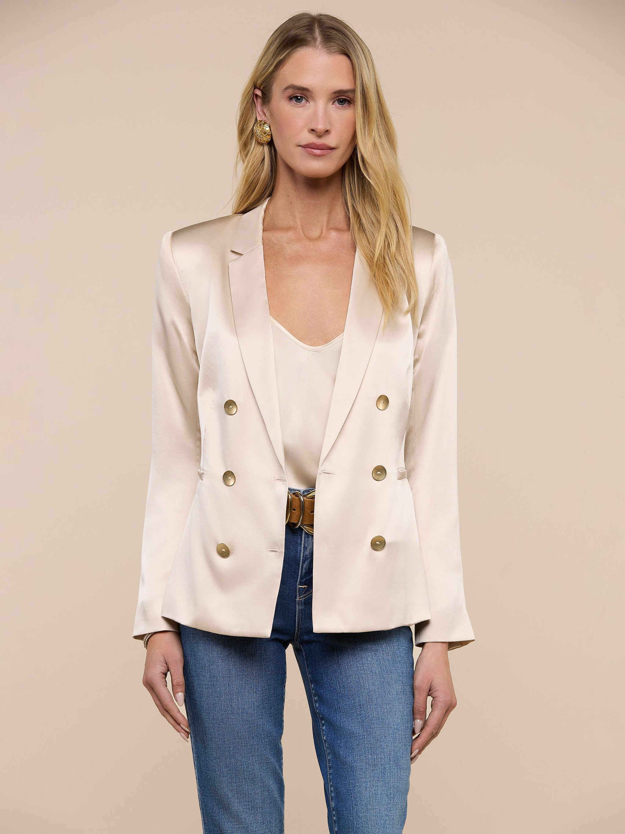 A woman wearing the Colin Silk Blazer in champagne over a matching top and blue jeans stands facing forward against a plain white background.