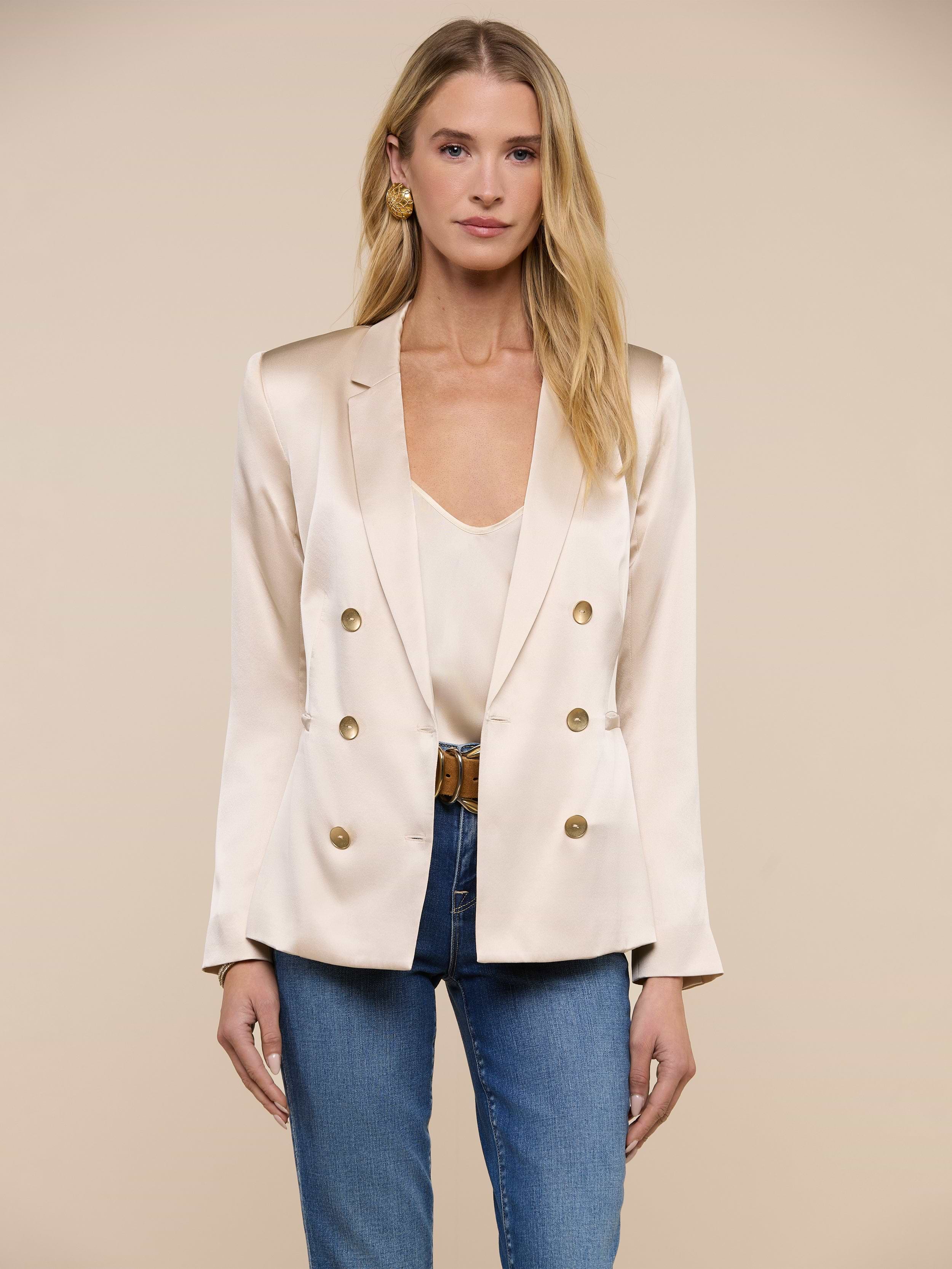 A woman wearing the Colin Silk Blazer in champagne over a matching top and blue jeans stands facing forward against a plain white background.