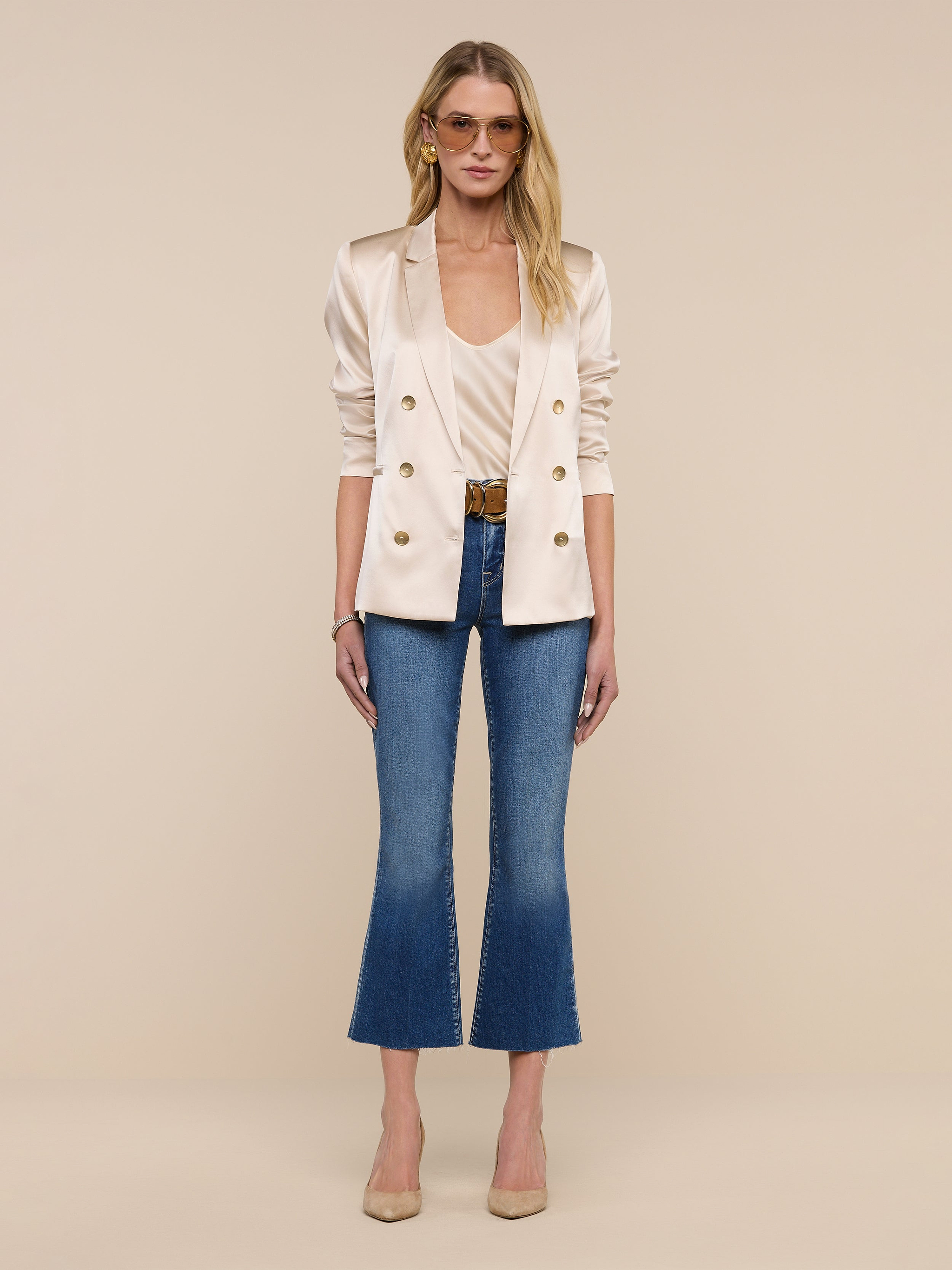 A woman stands facing forward against a plain white background, wearing the Colin Silk Blazer in champagne, a matching top, cropped blue jeans, and beige heels.