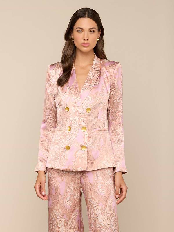 A woman wearing the Colin Silk Blazer in a pink paisley print with gold buttons and matching satin suit stands against a plain light background, looking forward with her arms relaxed at her sides.