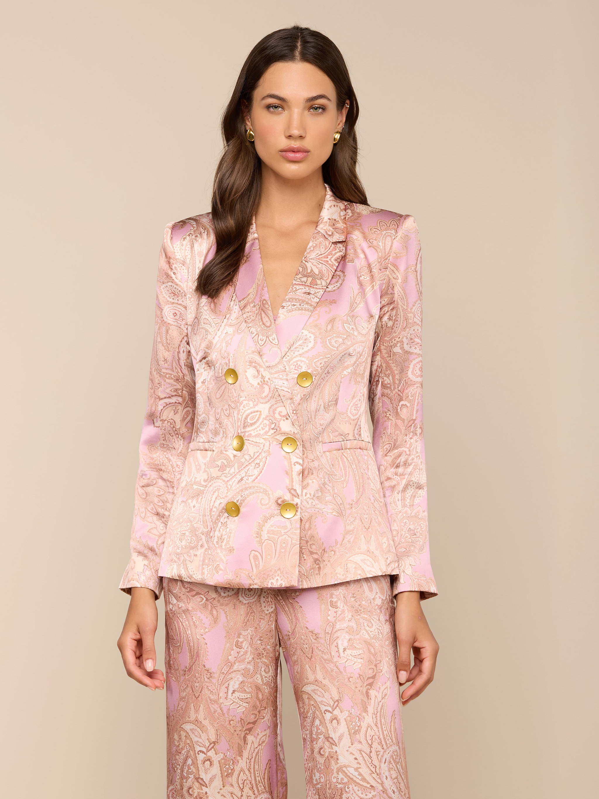 A woman wearing the Colin Silk Blazer in a pink paisley print with gold buttons and matching satin suit stands against a plain light background, looking forward with her arms relaxed at her sides.