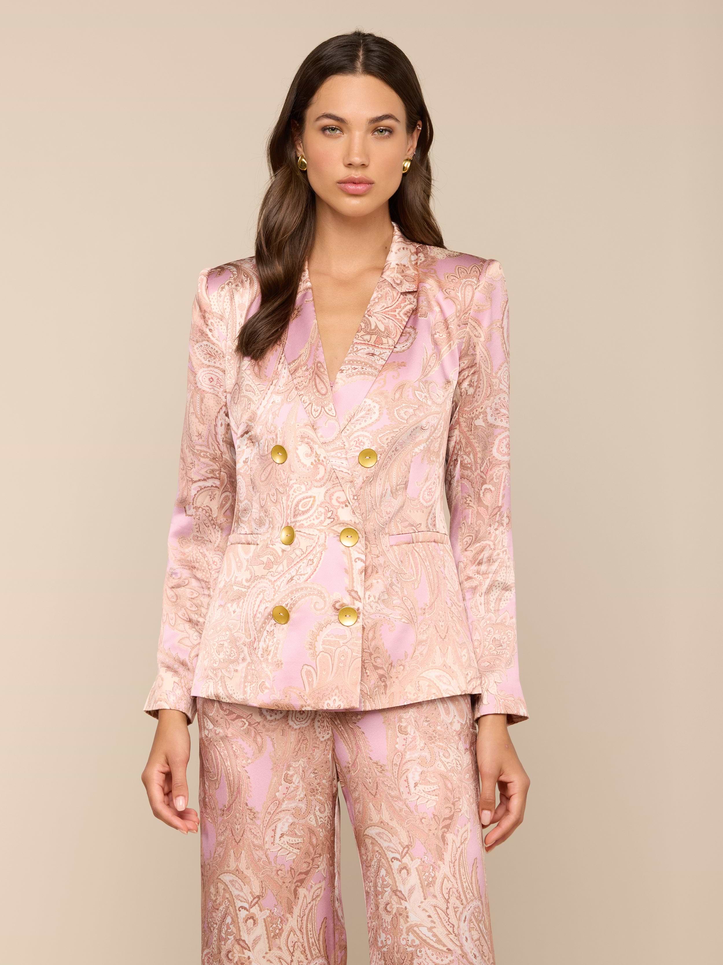 A woman wearing the Colin Silk Blazer in a pink paisley print with gold buttons and matching satin suit stands against a plain light background, looking forward with her arms relaxed at her sides.