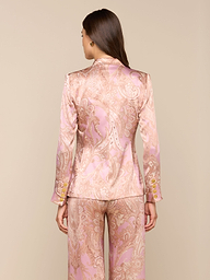 A woman stands facing away, wearing the Colin Silk Blazer and wide-leg pants in a pink and gold paisley print silk charmeuse with long sleeves, set against a plain light background.
