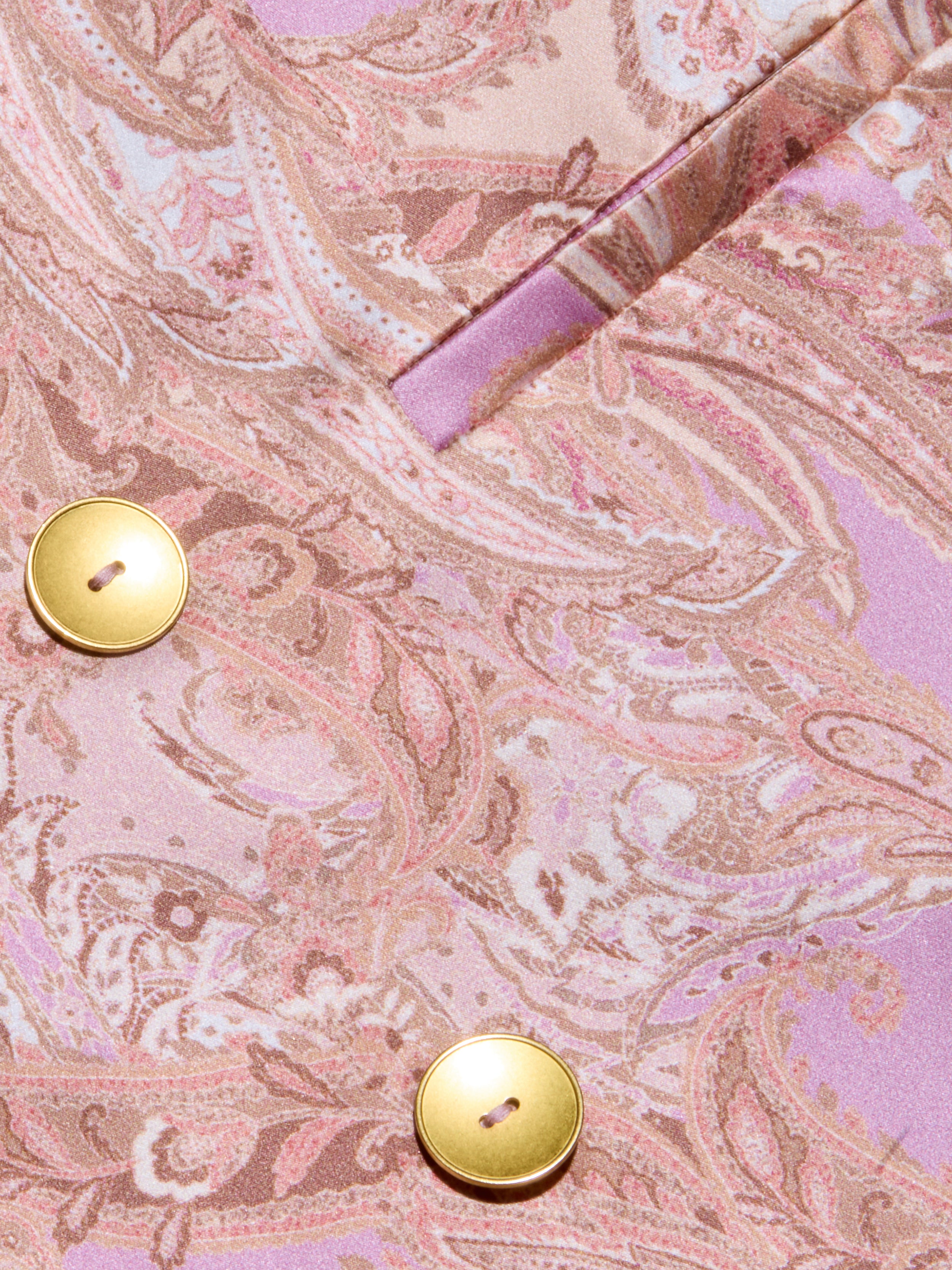 Close-up of the Colin Silk Blazer, featuring pink and beige paisley print silk charmeuse fabric with two shiny gold buttons and a fabric fold near the top right corner.
