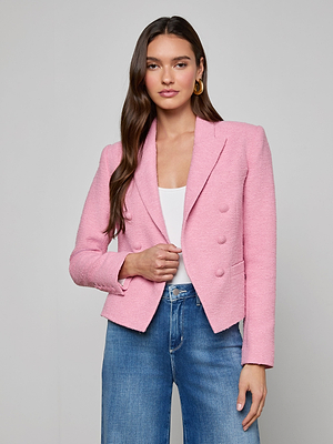 A woman with long brown hair wears the Brooke Tweed Blazer in pink over a white top and blue jeans, standing against a plain light gray background and looking at the camera with a neutral expression.
