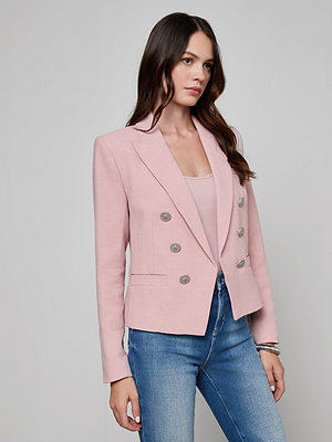 A woman with long brown hair wears the Brooke Open-Front Blazer in pale pink over a pink top and blue jeans, standing against a plain light gray background.