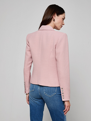 A woman with straight brown hair stands with her back to the camera, wearing the Brooke Open-Front Blazer in pale pink with silver sleeve buttons and blue jeans against a plain light gray background.