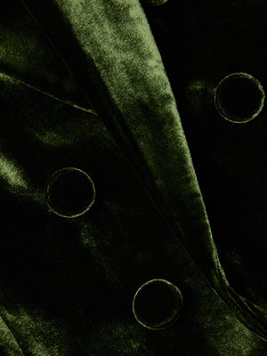 Close-up of the Brooke Velvet Blazer by L'AGENCE, crafted in dark green silk-infused velvet with a soft, shiny finish and accented by several large, round velvet-covered buttons.