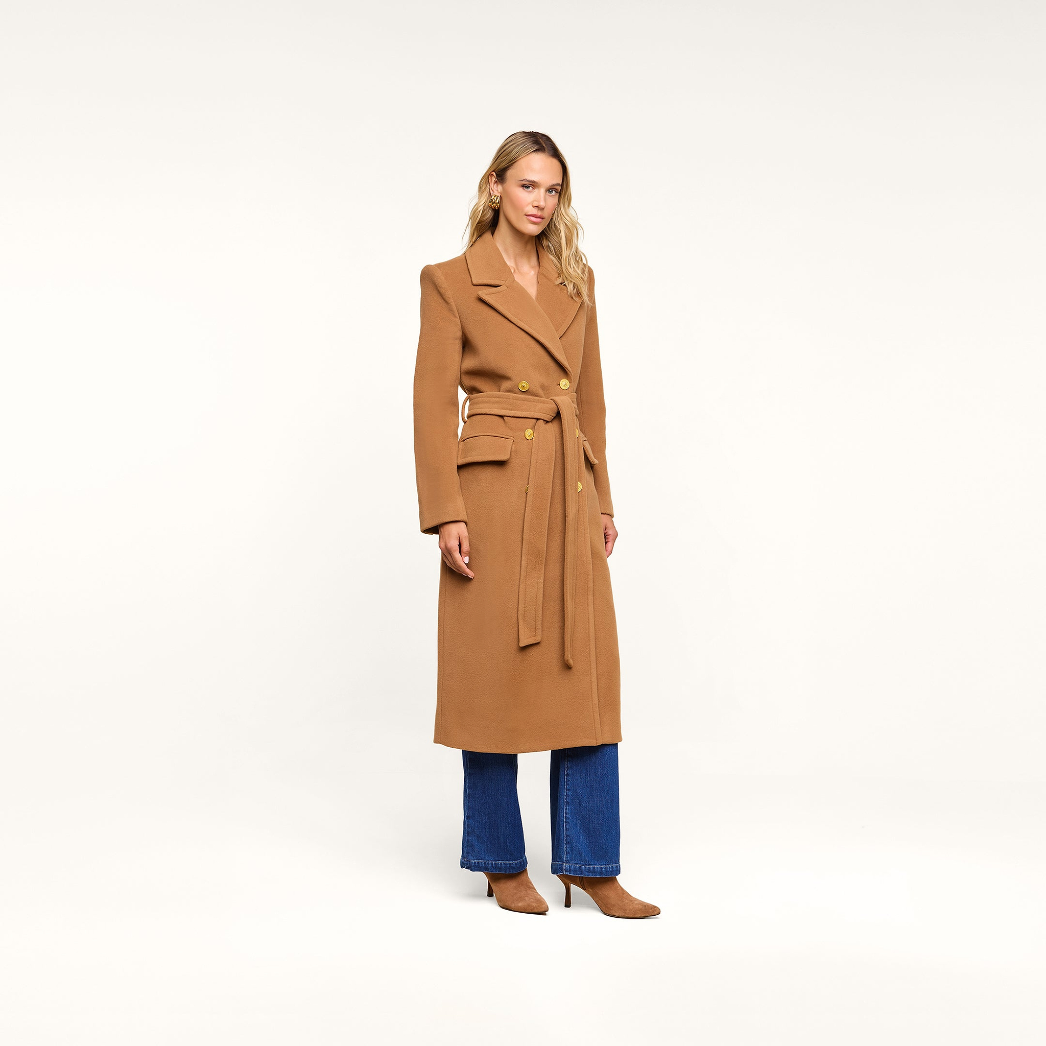 A person wearing the Kolina Long Coat, styled with blue jeans and tan heels, stands against a plain white background.