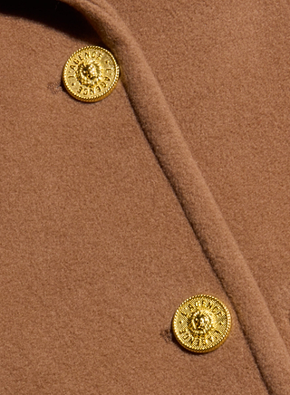 Close-up of the Kolina Long Coat in cognac brown Italian wool, showcasing two shiny gold buttons adorned with an embossed lion head design—capturing the essence of a timeless power coat.