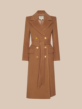 The Kolina Long Coat, crafted in a rich cognac brown Italian wool, features a double-breasted design with gold buttons, front pockets, a waist tie belt, and wide lapels. Shown against a plain beige background, this coat embodies timeless sophistication and statement style.