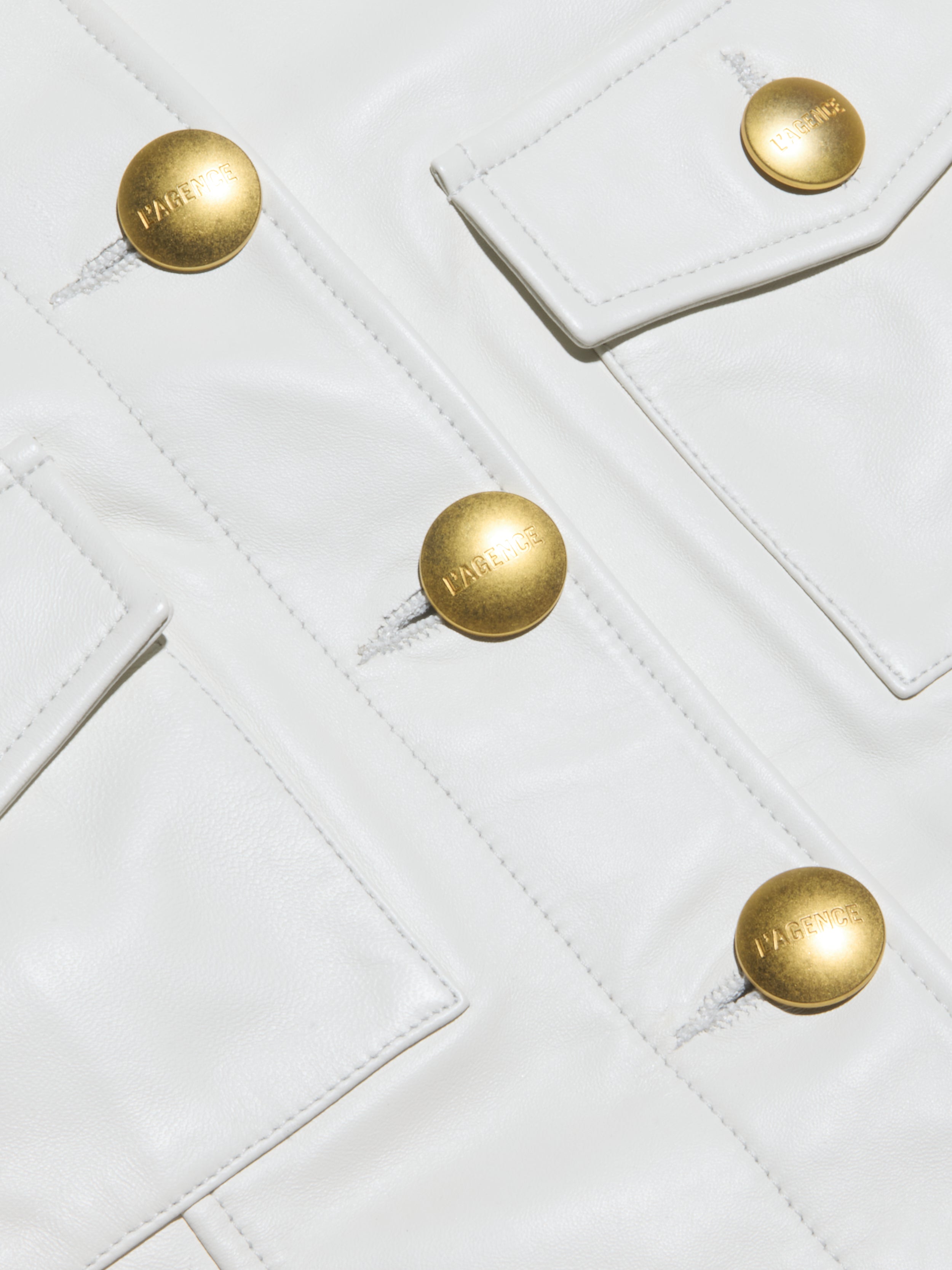 Close-up of the Kumi Cropped Leather Jacket, crafted from luxurious white lambskin leather and featuring gold buttons embossed with the word “FABRIQUE” as well as elegant flap pockets.