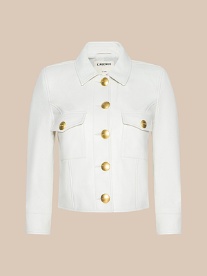The Kumi Cropped Leather Jacket, made from soft lambskin leather, features long sleeves, front flap pockets, and large gold buttons, displayed against a beige background.