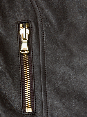 Close-up of the L'AGENCE Lyric Leather Peplum Jacket in dark brown lambskin, highlighting its gold zipper and fine texture—chic moto-inspired detailing for a feminine edge.