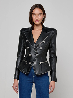 A woman with straight brown hair and a neutral expression models the L'AGENCE Ottilie Leather Blazer—an Italian lambskin piece with silver buttons and front zippers—paired with blue jeans against a plain background, expressing effortless power dressing.