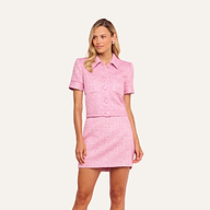 A woman wearing the Chita Tweed Jacket—a pink cropped tweed jacket with short sleeves—paired with a matching mini skirt, standing against a plain light background.