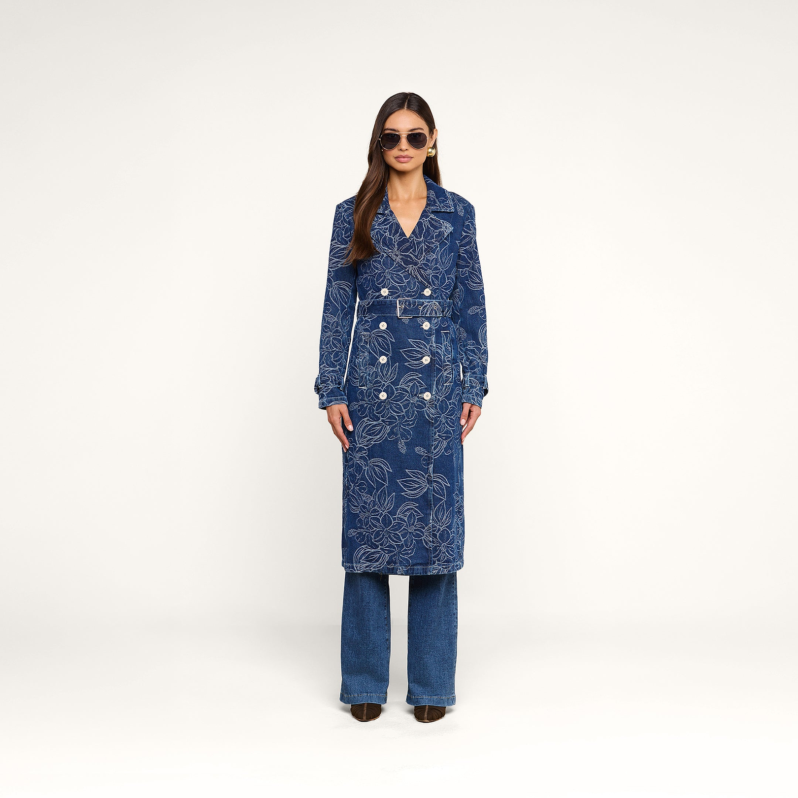 A person wearing the Bradley Trench Coat over blue pants and heeled shoes, with sunglasses, stands against a plain white background.
