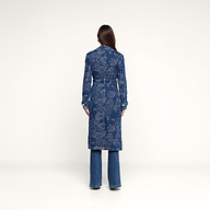 A person stands facing away, wearing the Bradley Trench Coat—a long blue floral jacquard trench coat—and blue jeans, against a plain white background.