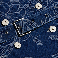 Close-up of the blue floral jacquard denim fabric with white buttons, metal grommets, and a square metal buckle from the Bradley Trench Coat.