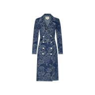 The Bradley Trench Coat is a long blue floral jacquard denim trench coat featuring a double-breasted front, wide collar, button details, waist belt, and long sleeves, displayed on a plain white background.