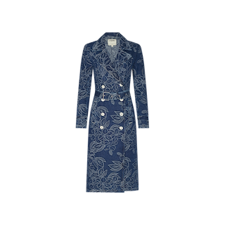 The Bradley Trench Coat is a long-sleeve, double-breasted blue denim trench coat featuring a striking floral jacquard pattern, white buttons, and a matching belt, displayed on a plain white background.