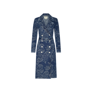 The Bradley Trench Coat is a long, blue denim trench coat made from luxurious floral jacquard fabric, designed with double-breasted buttons, notched lapels, and a coordinating belt, shown against a plain white background.