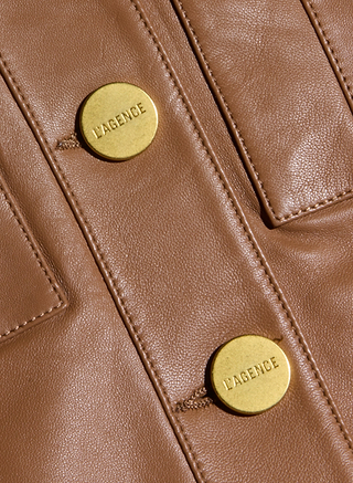 Close-up of the Deidra Cropped Leather Jacket in brown leather, designed with two gold LAGENCE-engraved buttons, visible stitching, and defined pocket seams.