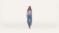 A woman stands against a plain white background, wearing a pink floral blouse, high-waisted blue jeans, and beige heeled sandals. She looks slightly to the side with her hands at her sides.