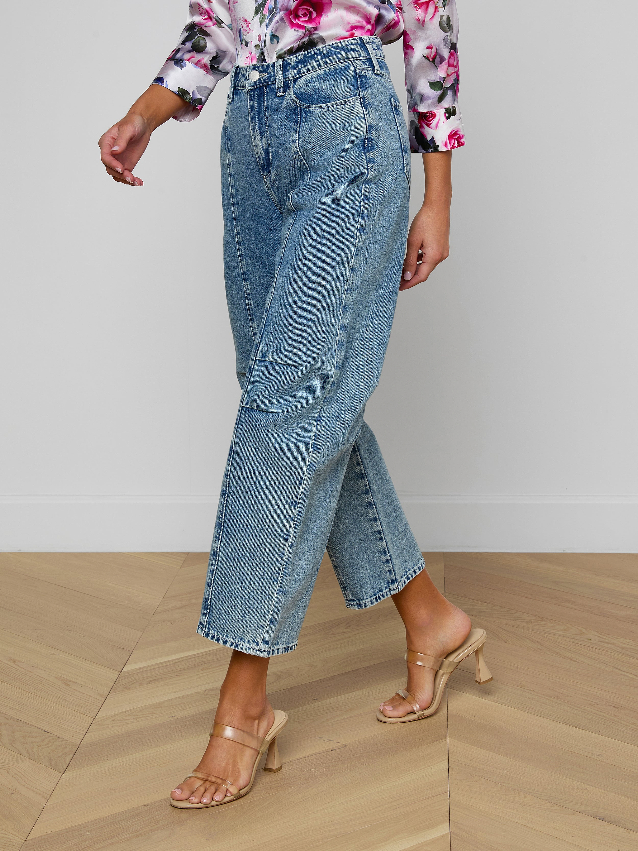 Person wearing Reba Rodeo Jean in light blue high rise denim paired with a floral long-sleeve top and beige heeled sandals, standing against a plain white background. Only lower body is visible.