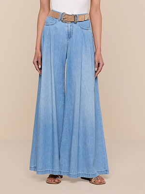 Someone wearing the Dariela Wide-Leg Jean in light blue featherweight denim with deep pleats, paired with a tan belt, white top, and brown sandals, standing against a neutral beige background.