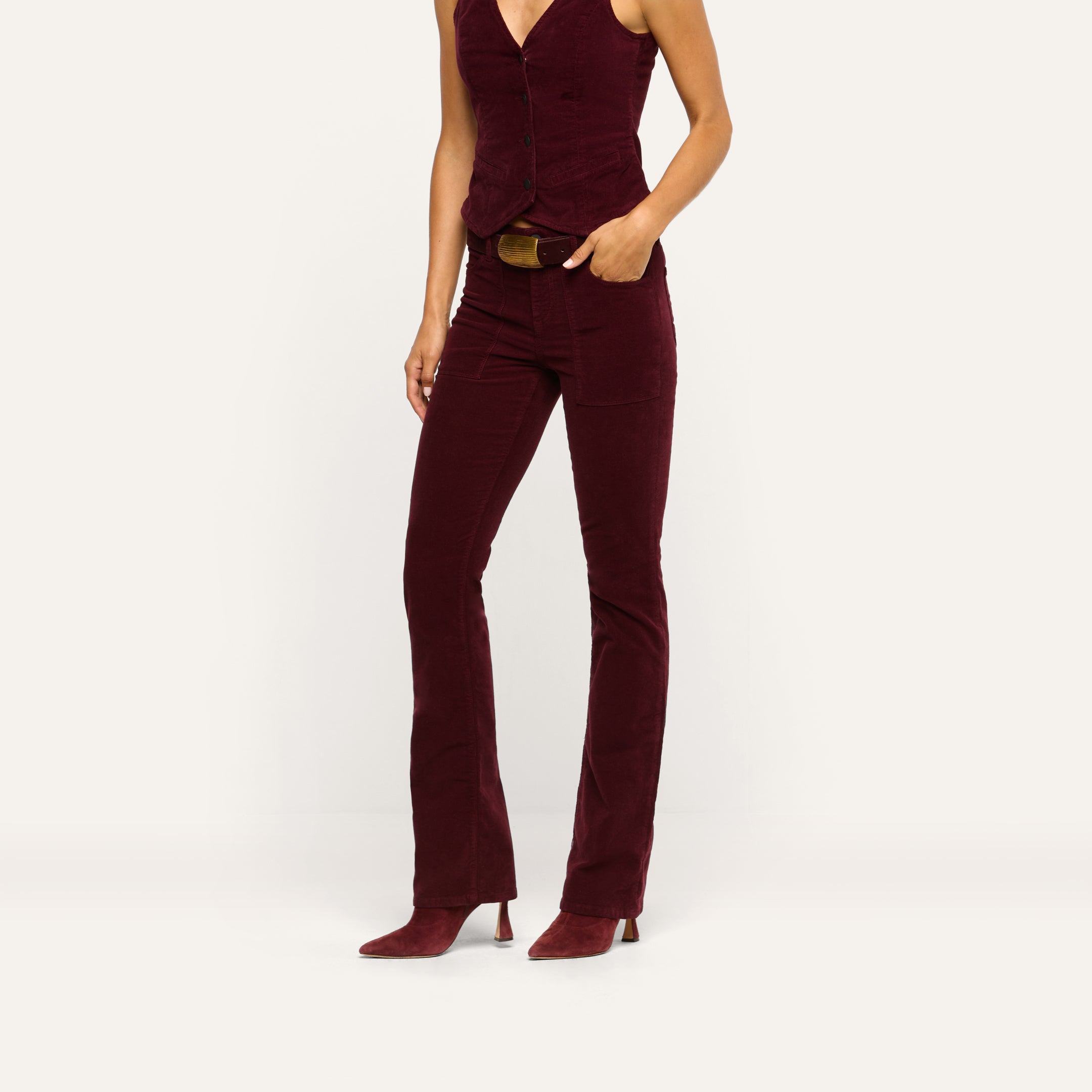 A person wearing Saffia Corduroy Pant high-rise stretch corduroy trousers with patch pockets, a matching button-down vest, and pointed-toe heels in a deep wine color.