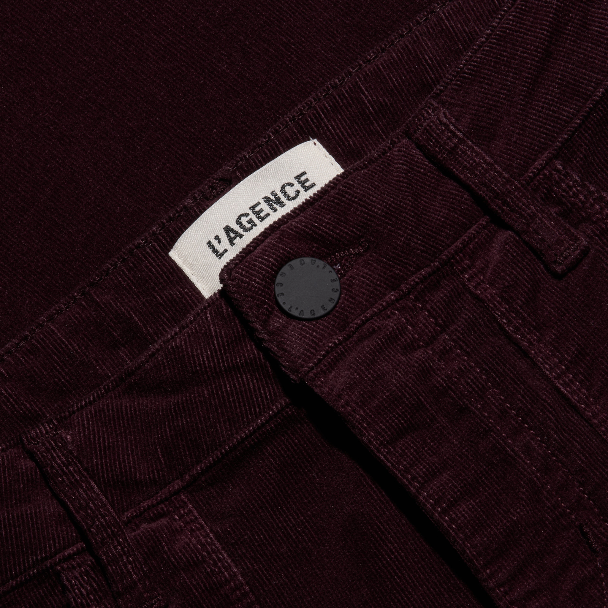 Close-up of the waistband of the burgundy Saffia Corduroy Pant, a slim-straight stretch style featuring a button closure and a brand label.