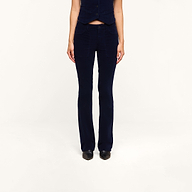 A person stands facing forward with their hands by their sides, wearing the Saffia Corduroy Pant in dark blue—a high-rise, flared style crafted from stretch corduroy—paired with a matching sleeveless vest against a plain white background. Their head is not visible in the image.