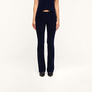A person, visible from the shoulders down, stands facing forward against a plain light background, wearing the Saffia Corduroy Pant—a pair of dark blue high-rise flared pants with front pockets—styled with a matching vest.