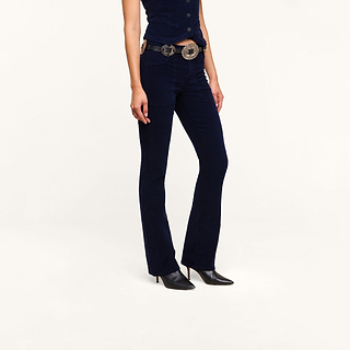 Wearing the Saffia Corduroy Pant in dark blue, paired with a matching vest, a decorative belt featuring large buckles, and black pointed-toe heeled shoes, a person stands against a plain white background.