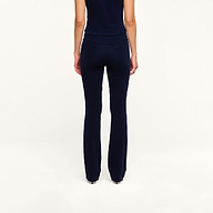 A person stands facing away from the camera, wearing a navy blue sleeveless top and the Saffia Corduroy Pant in a high-rise, flared silhouette, against a plain white background.