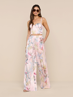 A woman wearing sunglasses, a sleeveless crop top, and Lillian Satin Wide-Leg Pants with a pink palm leaf print stands against a beige background.