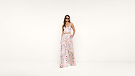 Woman wearing sunglasses and a pastel floral two-piece outfit with a crop top and wide-leg pants, standing against a plain white background.