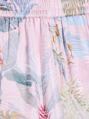 Close-up of the Lillian Satin Wide-Leg Pant in light pink jacquard satin, featuring a pastel palm leaf print and gathered elastic at the top. The slightly shiny fabric adds elegance to this ultra-wide leg design.