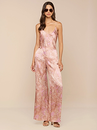 Une femme pose avec assurance sur un fond neutre, portant des lunettes de soleil et le pantalon large en soie Pilar à imprimé paisley mauve, avec des bretelles spaghetti pour un look chic.