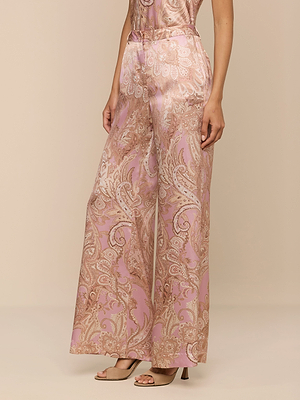 Wearing the Pilar Silk Wide-Leg Pant featuring a pink and beige paisley print, paired with open-toed nude heels, a person stands against a beige background with their upper body partially out of frame.