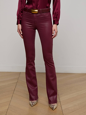 A person stands on a wooden floor wearing L'AGENCE Ruth Coated Straight-Leg Jeans, a matching satin blouse, a wide belt with a gold buckle, and pointed-toe snakeskin shoes. The image is cropped at the shoulders.