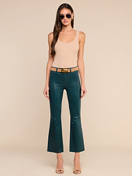 Une femme se tient debout devant un fond beige ; elle porte des lunettes de soleil, un haut sans manches beige, des sandales à talons beiges et le « Kendra Coated Cropped Flare Jean » — un jean évasé court à taille haute de couleur bleu sarcelle, muni dune ceinture.